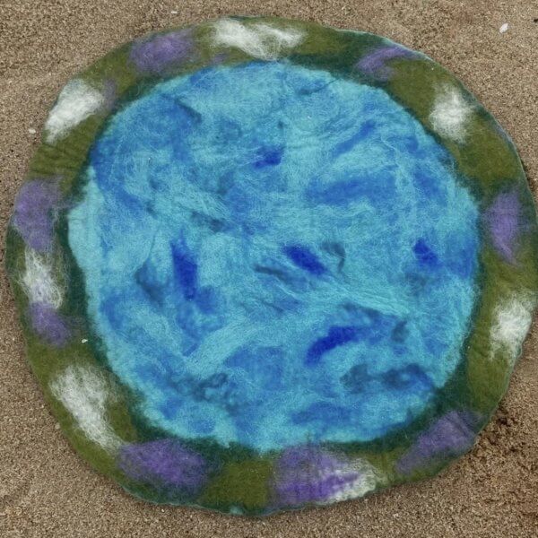 Round felt rug with a bright blue center and a green border accented by purple and white spots on sandspace relief around it.