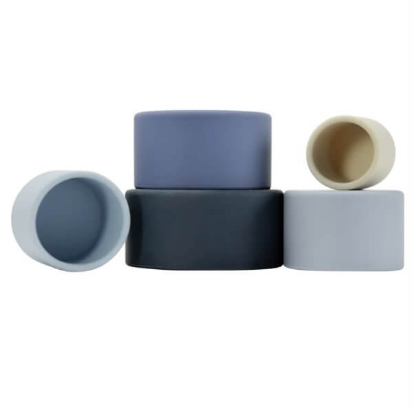 Blue silicone stacking cups | Bambino Eco Toys Stack of four small cylindrical silicone storage containers in muted blue and beige tones on a white background, arranged in a tiered stack with one resting on its side.