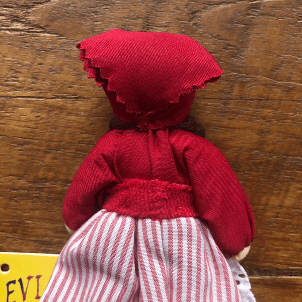 Summer girl Evi waldorf doll natural materials | Bambino Eco Toys Back view of a red-dressed fabric doll with a striped white-and-red skirt, set against a wooden background.