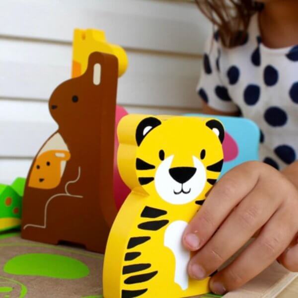 Kc puzzles wild animals chunky wooden puzzle | Bambino Eco Toys Child’s hand playing with a bright yellow tiger wooden toy among other animal shapes on a play surface.