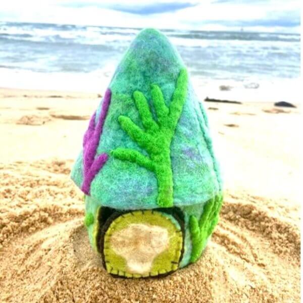 Colorful felt sea-shell house on sandy beach with the ocean in the background.