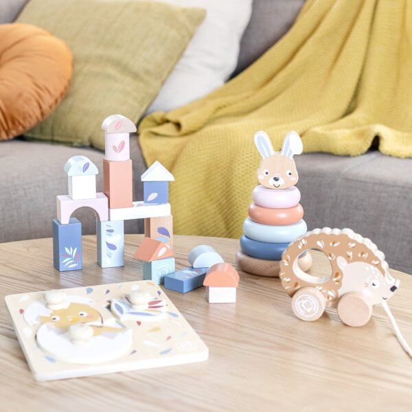 Pastel wooden block tower and bunny ring stacker on a light table with a yellow throw in the background.